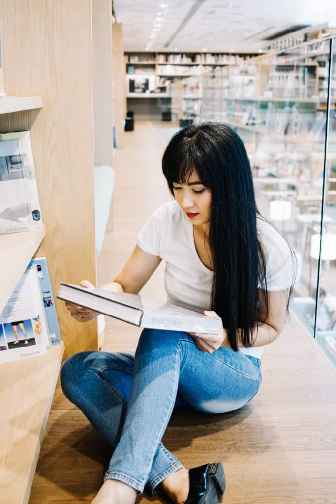 Girl reading a study book on the floor in a library.